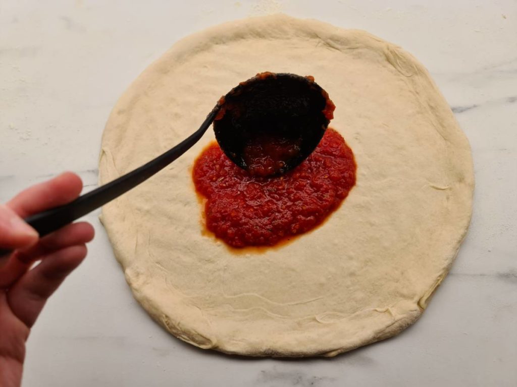 Ladeling pizza sauce in the center of the pizza