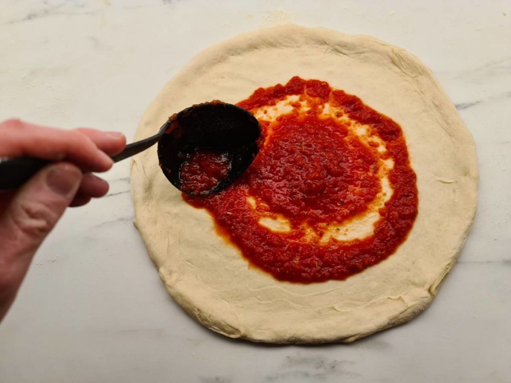 Spreading tomato sauce in a circular motion from the center to the rim